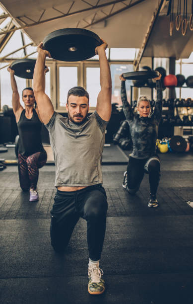 two young fitness women exercise with weights with personal trainer in the gym